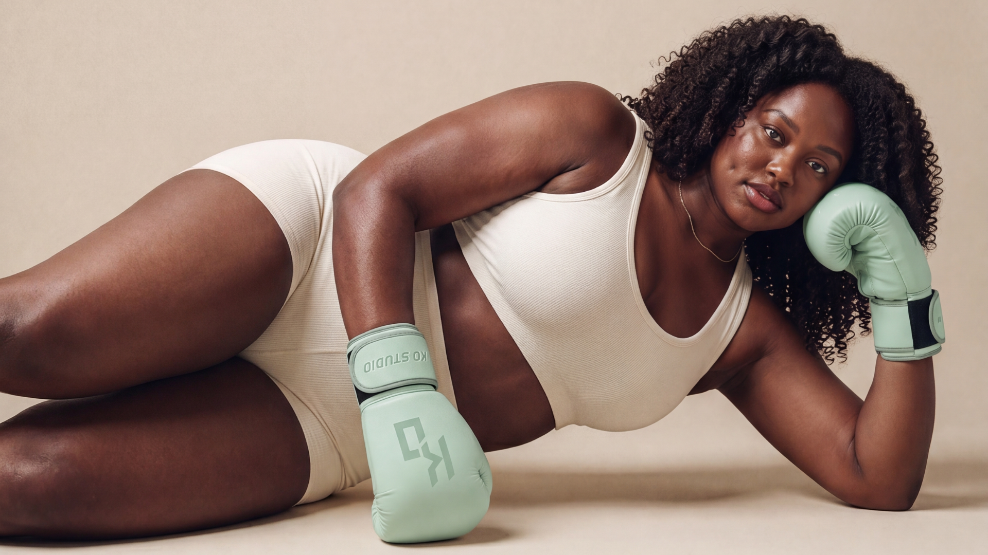 Woman in a sports bra and shorts wearing mint KO Studio boxing gloves, illustrating what to wear to a boxing class